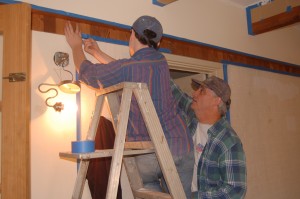 Rick Howard (right) and his son put up masking tape in preparation for painting the walls.